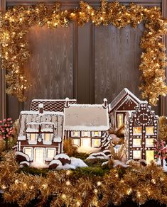 lighted gingerbread houses in front of a wooden wall with wreath and lights on it