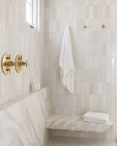 a white tiled bathroom with gold faucet and towel racks on the wall next to it