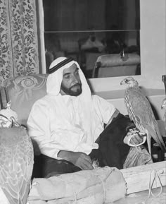 an old photo of a man sitting on a couch with two birds in front of him