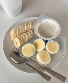 an egg, sliced bananas and yogurt are on a white plate with silverware