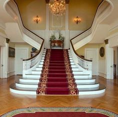 a staircase with red carpet and chandelier in the center, leading up to two rooms