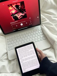 a person is holding an electronic device in front of a laptop computer on a bed