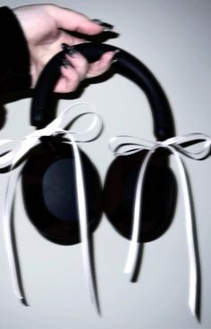 a pair of black headphones being held by someone's hand with white ribbon