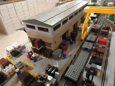 a model train station with people and trains on the tracks in front of it's depot