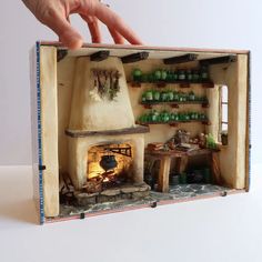 a hand is reaching into an open box with a fireplace in it and shelves on the wall