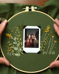 two hands holding up a green embroidered photo frame with yellow flowers and leaves on it