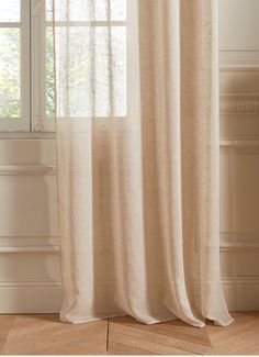 a white curtain hanging in front of a window next to a wooden floor and wall