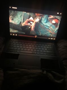 an open laptop computer sitting on top of a bed in the dark with its screen lit up