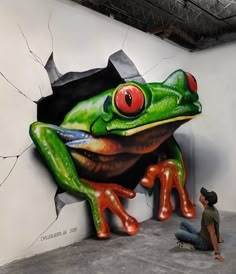 a man kneeling down in front of a large frog painted on the side of a wall