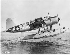 an old airplane flying over the ocean with people on it's wing and in the water