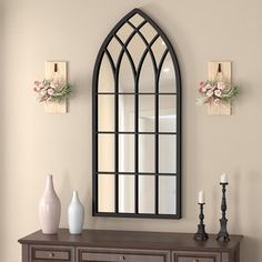 an arched mirror on the wall above a dresser with vases and candles in front of it