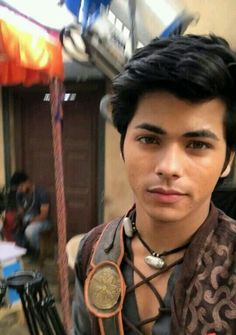 a young man is standing in front of a building with an ornate necklace on his neck