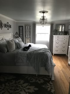 a cat laying on top of a white bed in a bedroom next to a window