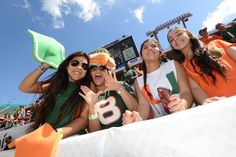 some girls in green and orange shirts at a football game with their hands up to the camera