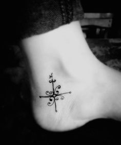 a black and white photo of a foot with a cross tattoo design on it's side