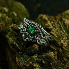 a green ring sitting on top of a mossy rock with leaves and vines around it