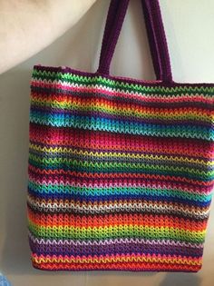 a multicolored crocheted tote bag hanging from a hook on a wall