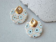 two white and blue ceramic earrings with gold accents on the earring hooks, sitting next to a rock