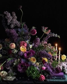 an arrangement of flowers and candles on a table with books in front of the candle