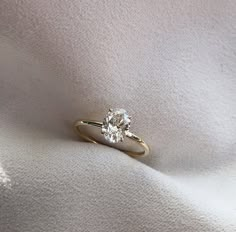 a gold ring with a single diamond on the top, sitting on a white cloth