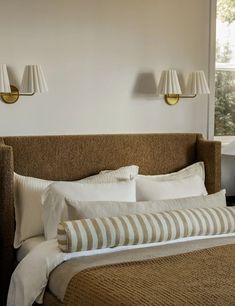 a bed with two lamps on the wall above it and some pillows in front of it