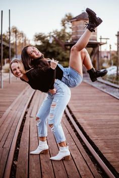 two young women are posing on a wooden platform with their legs in the air and one is holding another woman's leg