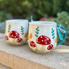 two coffee mugs with red mushrooms painted on them