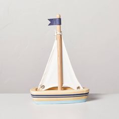 a small wooden sailboat with a blue flag on it's mast, sitting on a white surface