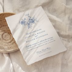 a white and blue wedding card sitting on top of a table next to a bowl