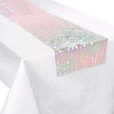 a white table cloth with pink and green sequins on the edge is shown