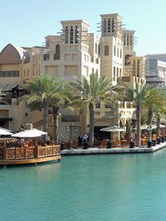 people are sitting at tables by the water in front of some buildings and palm trees