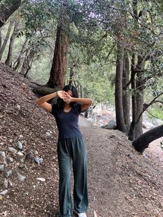 a woman standing in the middle of a forest with her hands on her head and eyes closed