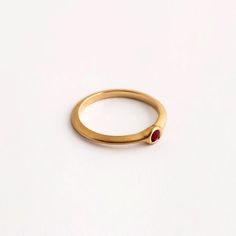 Our round ruby engagement gold ring is a dainty ring with a small ruby set within it. The ring is part of the 'Strings' ring family, a series of rings with a triangular profile and a small stone set in a variety of ways. They stack together gently, with small airy spaces between them, and can be suitable as engagement rings. The ring is made using traditional jewelry techniques to create a piece of jewelry that is classic and unique. It is elegant and comfortable to wear and will live with you h Formal Gold Stackable Ruby Rings, Ruby Ring With Round Band For Promise, Promise Ruby Ring With Birthstone, Gold Ruby Solitaire Birthstone Ring, Gold Ruby Birthstone Ring With Solitaire, Gold Ruby Birthstone Ring With Round Band, Ruby Solitaire Ring For Promise, Ruby Birthstone Ring For Promise Occasion, Gold Stackable Ruby Birthstone Ring