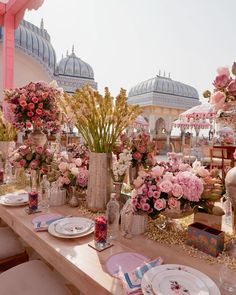 the table is set with pink and white flowers in vases, plates and napkins