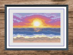 a cross stitch sunset with clouds and the sun setting in the distance, on a wooden surface