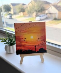 an easel sitting on a window sill in front of a painting with the sun setting