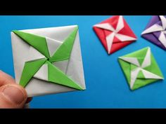 someone holding an origami piece in front of four different colored paper pieces on a blue background