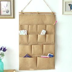 a wall hanging organizer with several pockets for books and magazines in front of some pictures on the wall