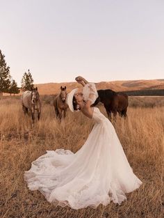 a woman in a wedding dress standing next to two horses on a dry grass field