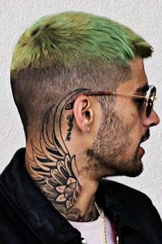 a man with green hair and tattoos on his face looking to the side while wearing glasses