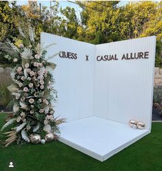 an outdoor display with flowers and shoes on the grass in front of a white wall