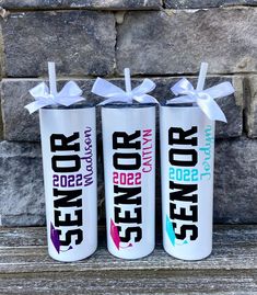 three personalized water bottles with ribbons tied around them on a wooden bench in front of a stone wall