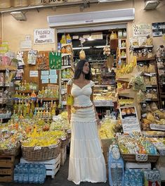 a woman standing in front of a store filled with fruits and vegetables