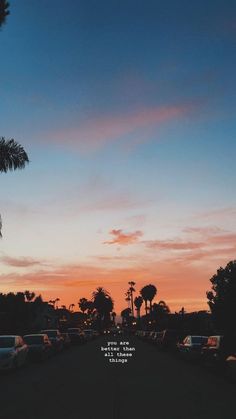 the sun is setting over a parking lot with cars parked on it and palm trees in the background