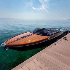 a wooden speed boat docked at a pier on the water with clear blue skies in the background