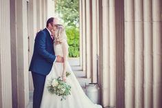 a bride and groom kissing in front of columns