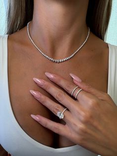 a woman wearing a diamond necklace and ring with her hands on her chest, posing for the camera