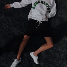 a person laying on the ground wearing white and green hoodie, black shorts and sneakers