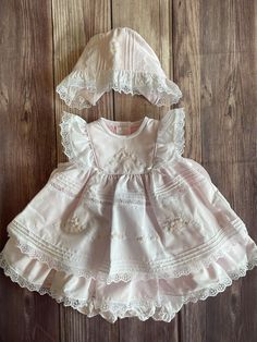 Sure to be a favorite! Your little one will receive so many compliments in this beautiful ensemble! Beautiful detailing in this stunning dress! Vintage inspired heirloom dress with white voile overlaying a pink lining!! A darling basket of flowers shadow stitched on the yolk with pearl accents, satin ribbon bows attached, piping trim around the yolk for a darling pinafore look, lace ruffle flutter sleeves, vertical pintucks on the layered skirt with lace accents, more embroidered flowers with pearl centers & another darling flower basket and pintucks with lace trim at the ruffle hem. Beautiful matching bonnet with pintucks, lace and embroidery details and ruffle trim with lace. Matching white bloomers White Bloomers, 3 Piece Dress, Smocked Bishop Dress, Vintage Baby Dresses, Heirloom Dresses, Basket Of Flowers, Vintage Baby Clothes, Satin Ribbon Bow, Lace Layers