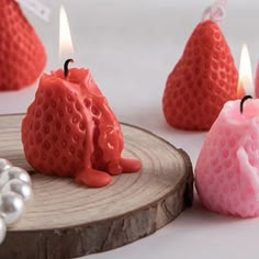 three strawberry shaped candles sitting on top of a wooden slice